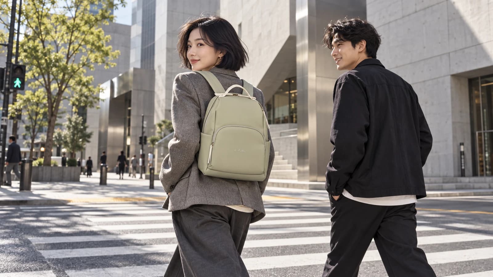 A woman wearing a sage backpack walks across a city street beside a friend